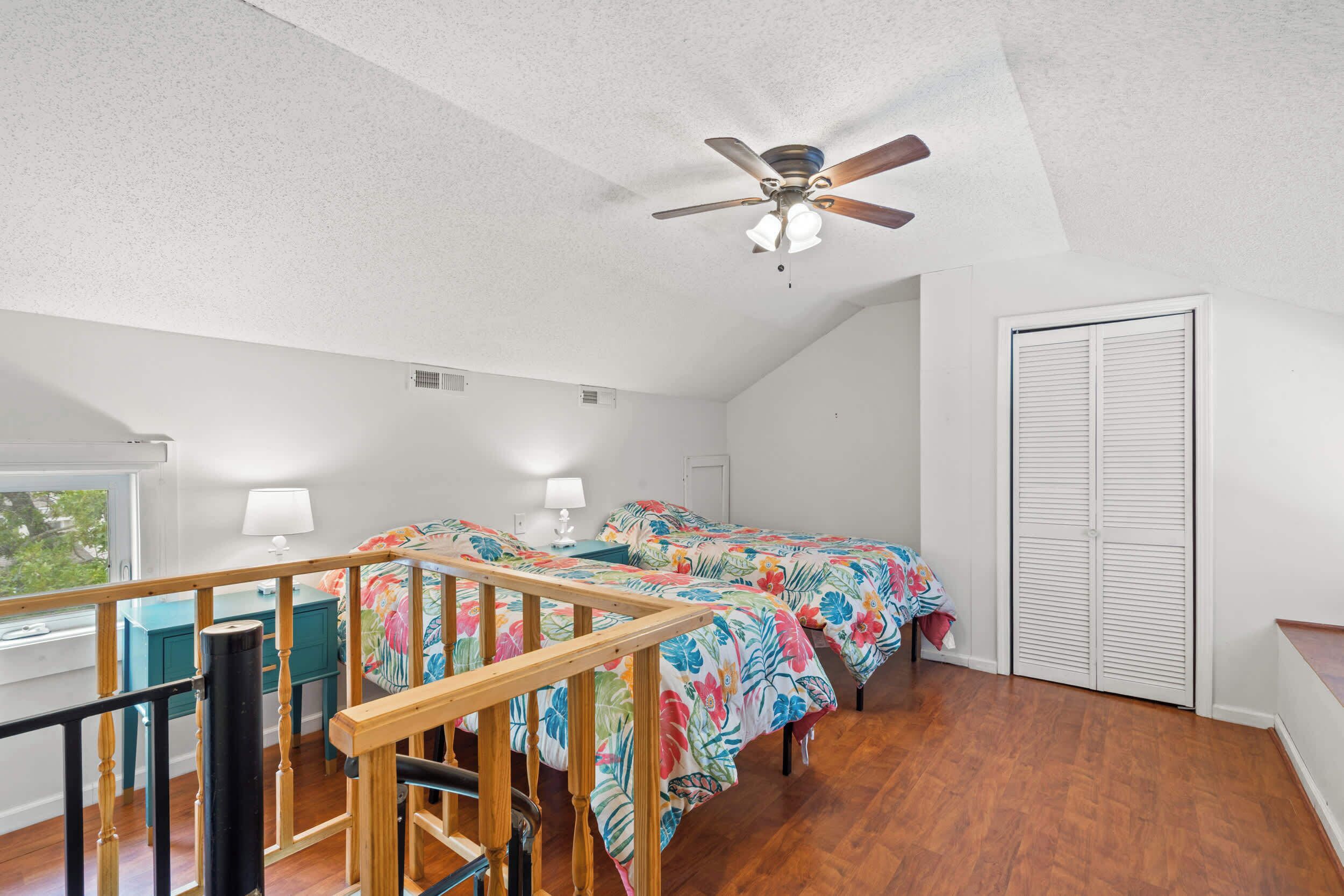 A bedroom with a wooden staircase, a ceiling fan, a window, and a closet.