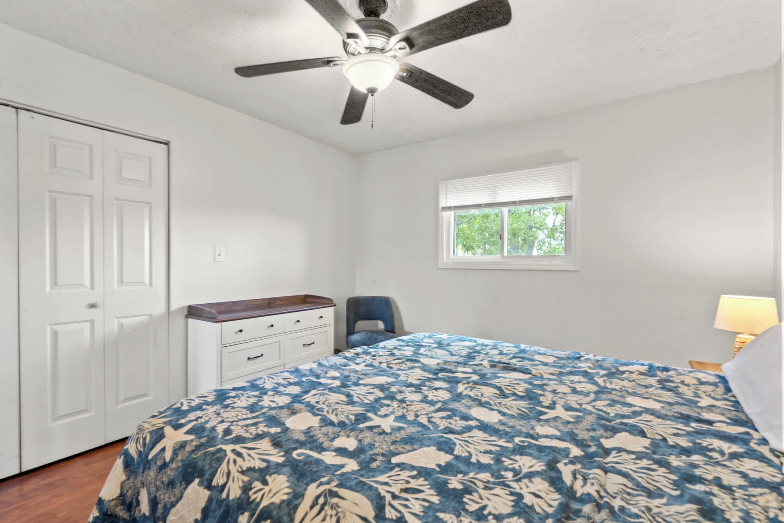 A bedroom with a bed, a ceiling fan, a window, a dresser, and a chair.