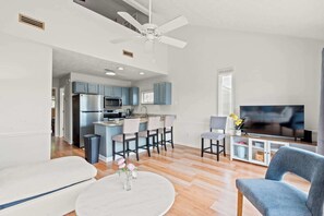 A modern living room with a flat-screen TV, a ceiling fan, and a dining area with bar stools. - Surfside Love Shack at Deer Creek (Myrtle Beach)