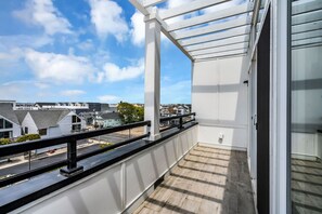 A balcony with a view of residential buildings, a wooden floor, and a white railing. - Luxury 3BR with Seaside Views Jersey Shore Gem (Seaside Heights)