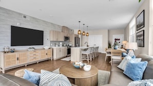 A modern living room with a large flat-screen TV, a wooden coffee table, and a sofa with blue cushions. - Luxury 3BR with Seaside Views Jersey Shore Gem (Seaside Heights)