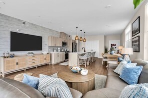 A modern living room with a large flat-screen TV, a wooden coffee table, and a sofa with blue cushions. - Luxury 3BR with Seaside Views Jersey Shore Gem (Seaside Heights)