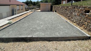 Un área pavimentada con un muro de piedra, un edificio pequeño con una escalera y un garaje.