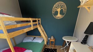 Una cama individual superpuesta con colchón verde, una mesita de noche pequeña, un escritorio blanco, una lámpara y una decoración de pared.