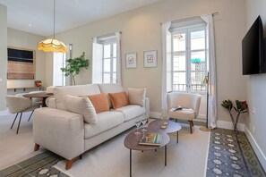Een moderne woonkamer met een bank, salontafel en stoelen, een eethoek met tafel en stoelen, en een groot raam met gordijnen.