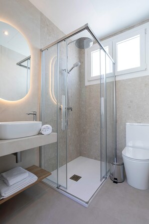 Een moderne badkamer met een douchecabine van glas, een wit wastafelmeubel en een toilet.