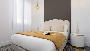 Ein modernes Hotelzimmer mit einem großen Bett, einem Nachttisch, einer Wandleuchte und einem Fenster mit durchsichtigen Vorhängen.