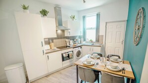 Une cuisine moderne avec des meubles blancs, une table à manger pour quatre personnes et un lave-linge.
