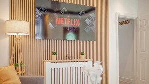 Un salon moderne avec un téléviseur fixé à un mur en bois, un canapé, une lampe et une petite table sur laquelle est posé un vase.