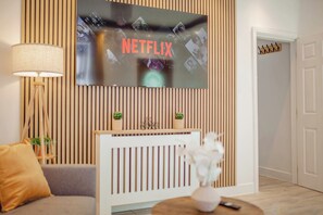Ein modernes Wohnzimmer mit an einer Holzwand montiertem Fernseher, einer Couch, einer Lampe und einem kleinen Tisch mit einer Vase.