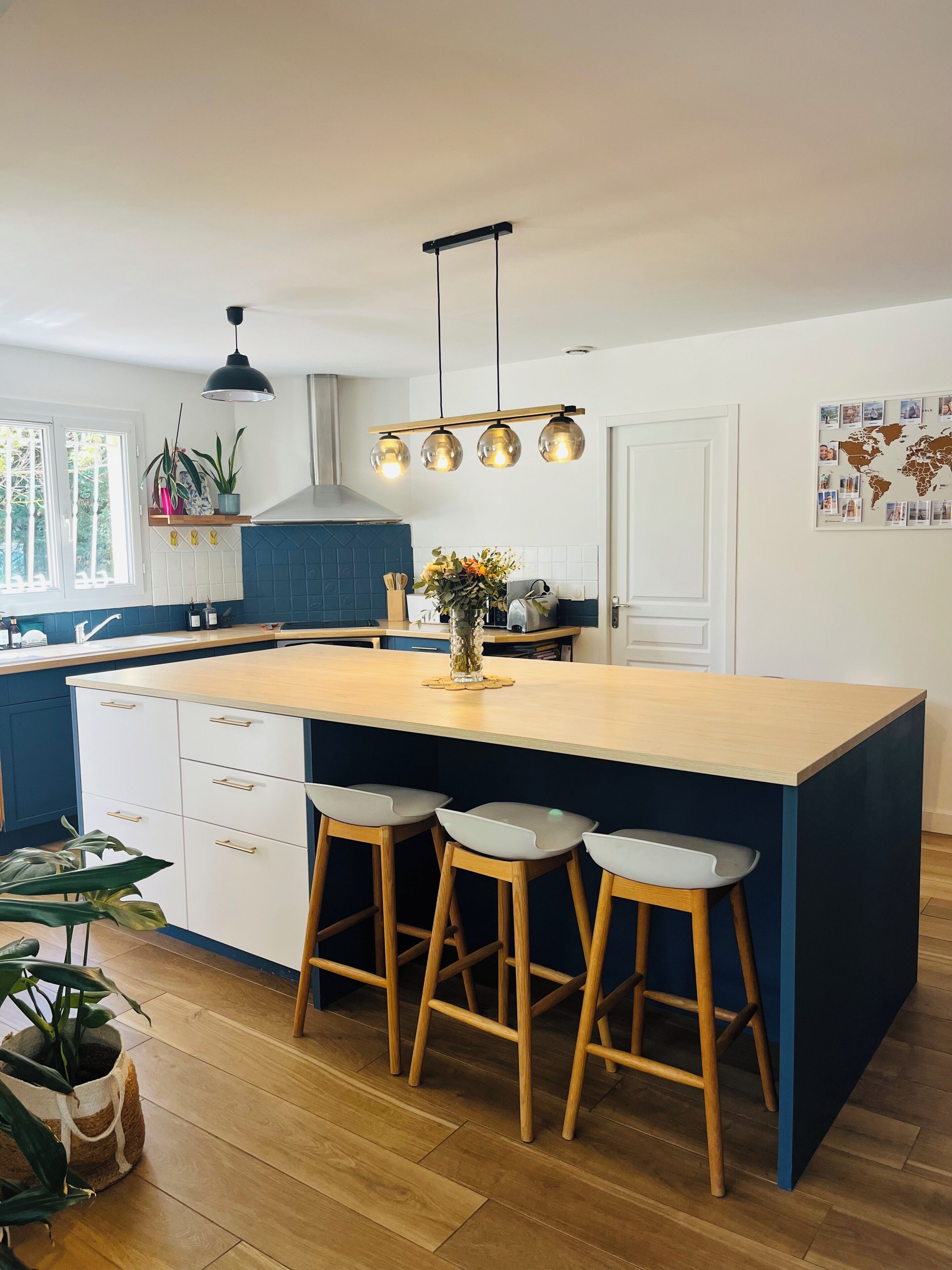 A kitchen with a central island, bar stools, a hanging light fixture, and a world map on the wall.