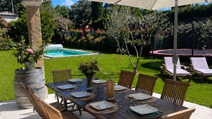 Une terrasse extérieure avec une table dressée pour le repas, entourée de fauteuils et d’un parasol.
