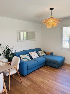 A modern living room with a blue sectional sofa, a dining table with chairs, a hanging rattan light fixture, and a large window. - La Villa des Anges, Provencal house with swimming pool and air conditioning - Aix en Provence (Aix-en-Provence)