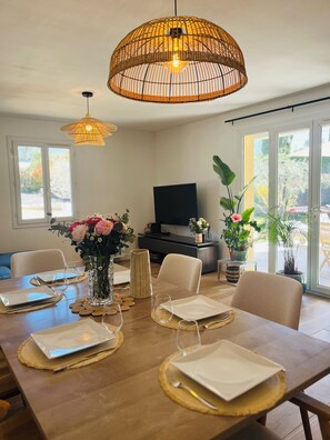 A dining area with a wooden table set for four, two hanging wicker lamps, a television, and potted plants. - La Villa des Anges, Provencal house with swimming pool and air conditioning - Aix en Provence (Aix-en-Provence)