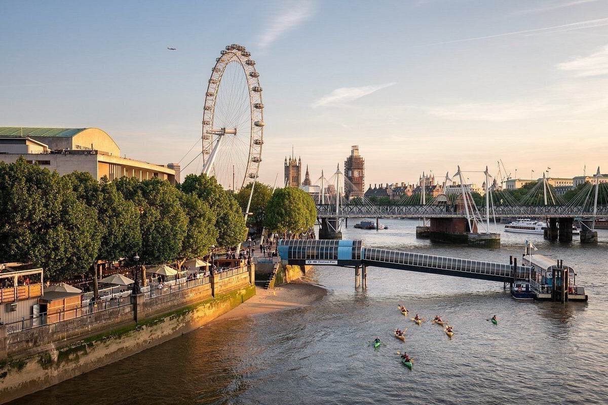 A river with a bridge, a Ferris wheel, and a historic building in the background.