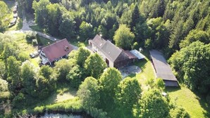 Vista aérea de una propiedad con una casa grande, un granero y un edificio más pequeño, rodeada de un bosque denso.