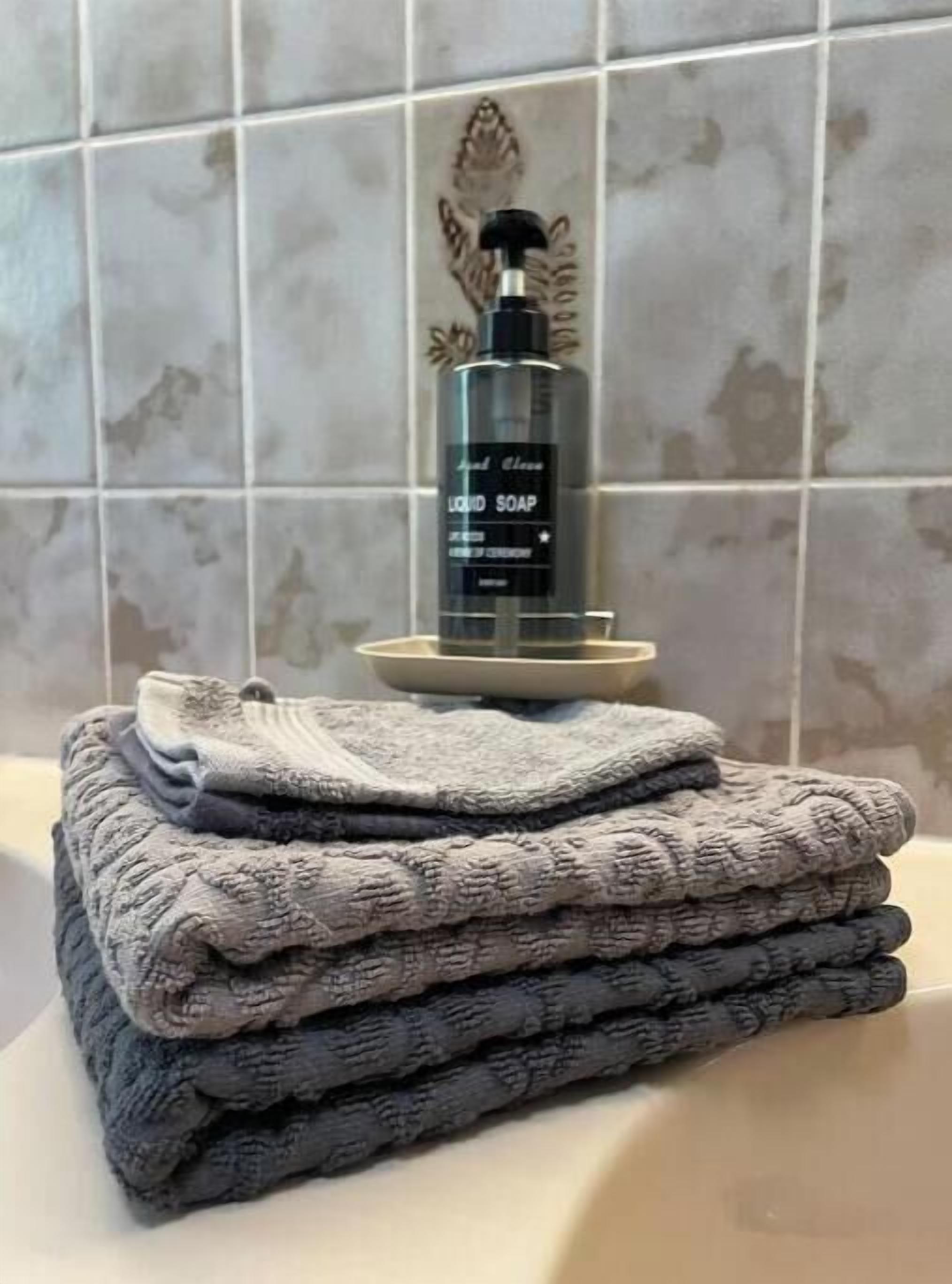 A bathroom with a stack of folded towels, a bottle of liquid soap, and a decorative tile backsplash.