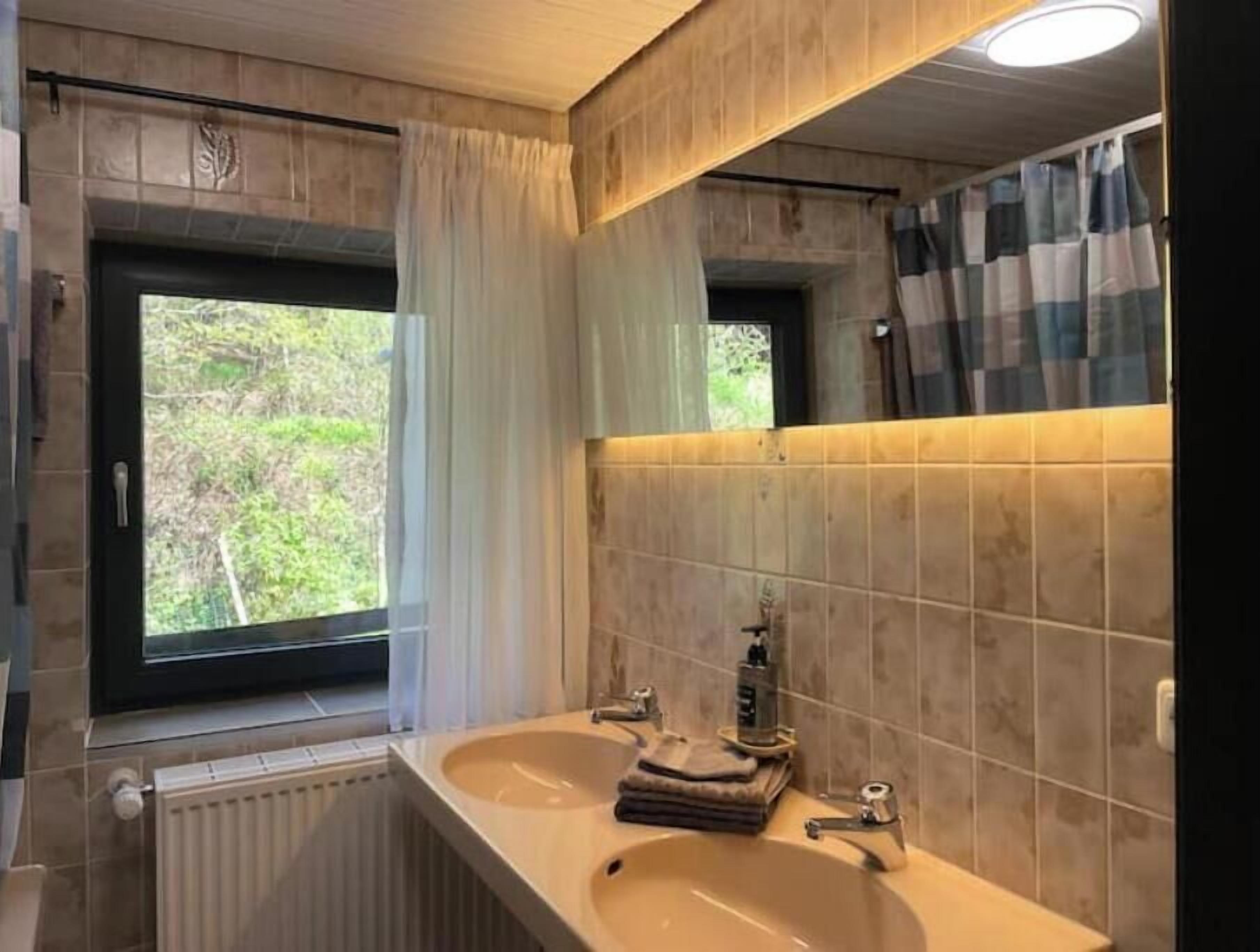 Un baño con dos lavamanos, una ventana con cortinas, un radiador y un espejo con una toalla a rayas.