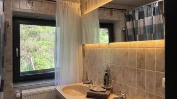 Un baño con dos lavamanos, una ventana con cortinas, un radiador y un espejo con una toalla a rayas.