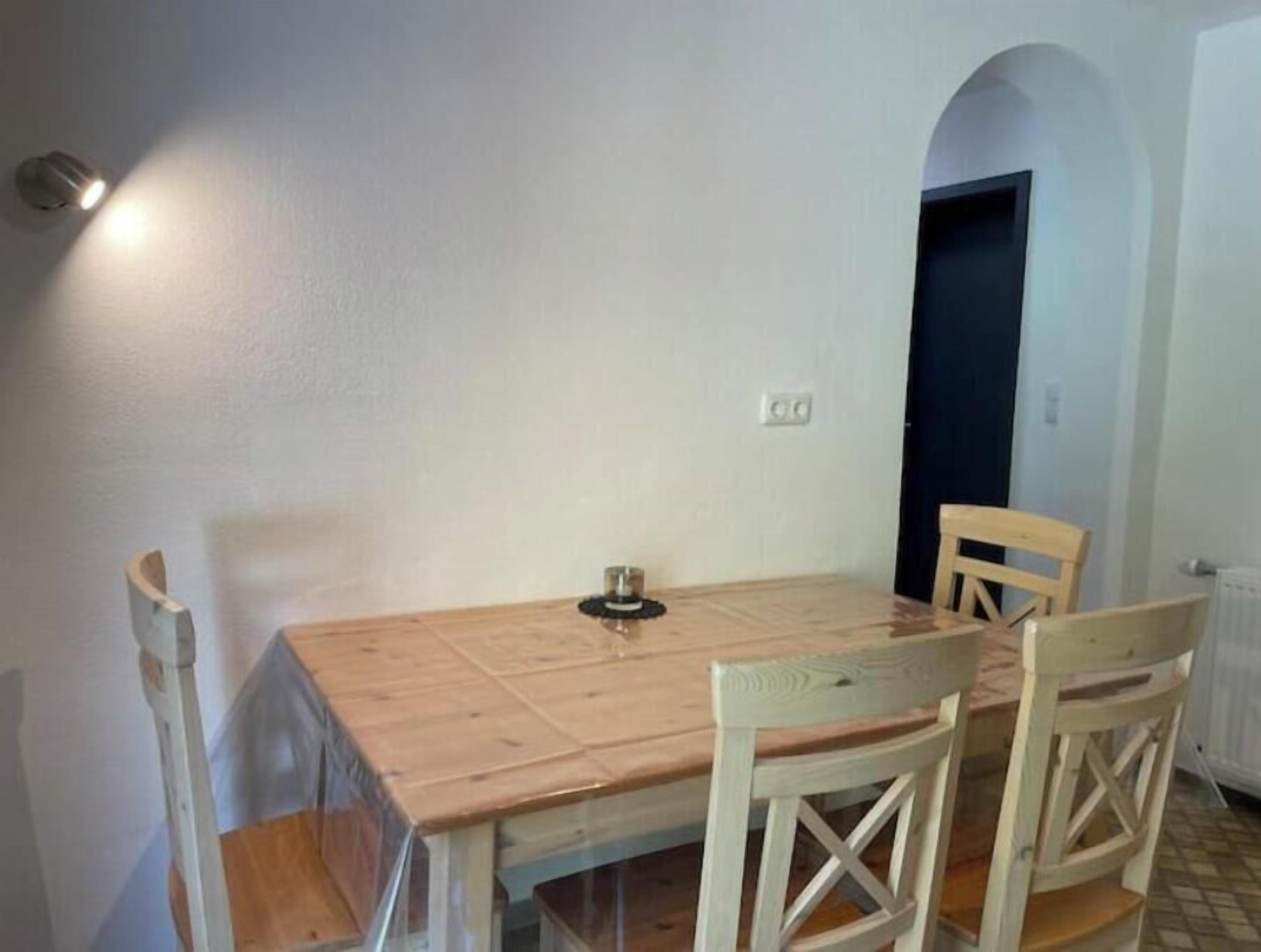 Een eethoek met een houten tafel en vier stoelen, een kleine tafellamp en een deur op de achtergrond.