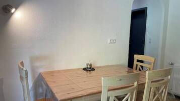 Een eethoek met een houten tafel en vier stoelen, een kleine tafellamp en een deur op de achtergrond.