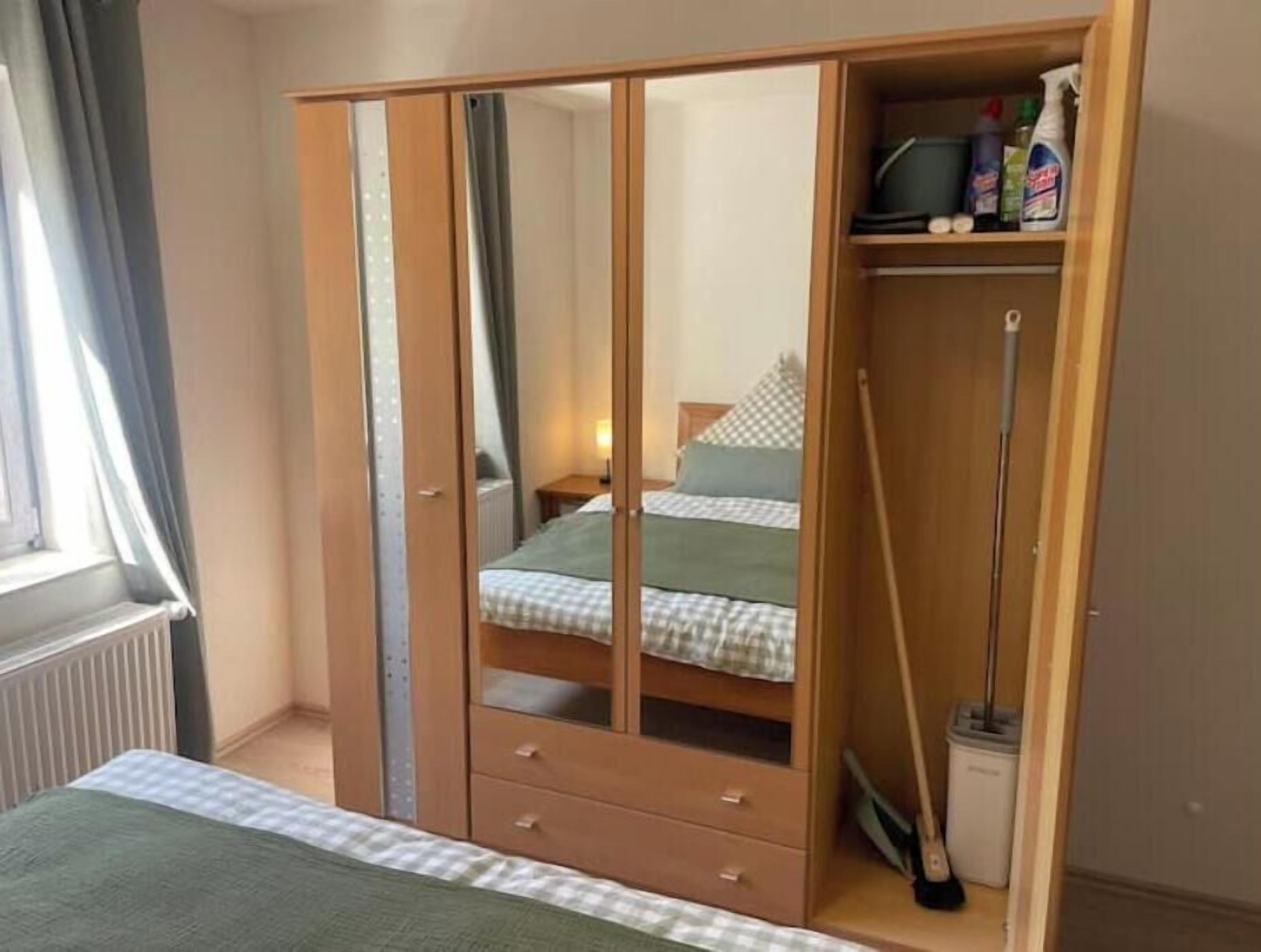 Un dormitorio con armario, cama, radiador y ventana con cortinas.