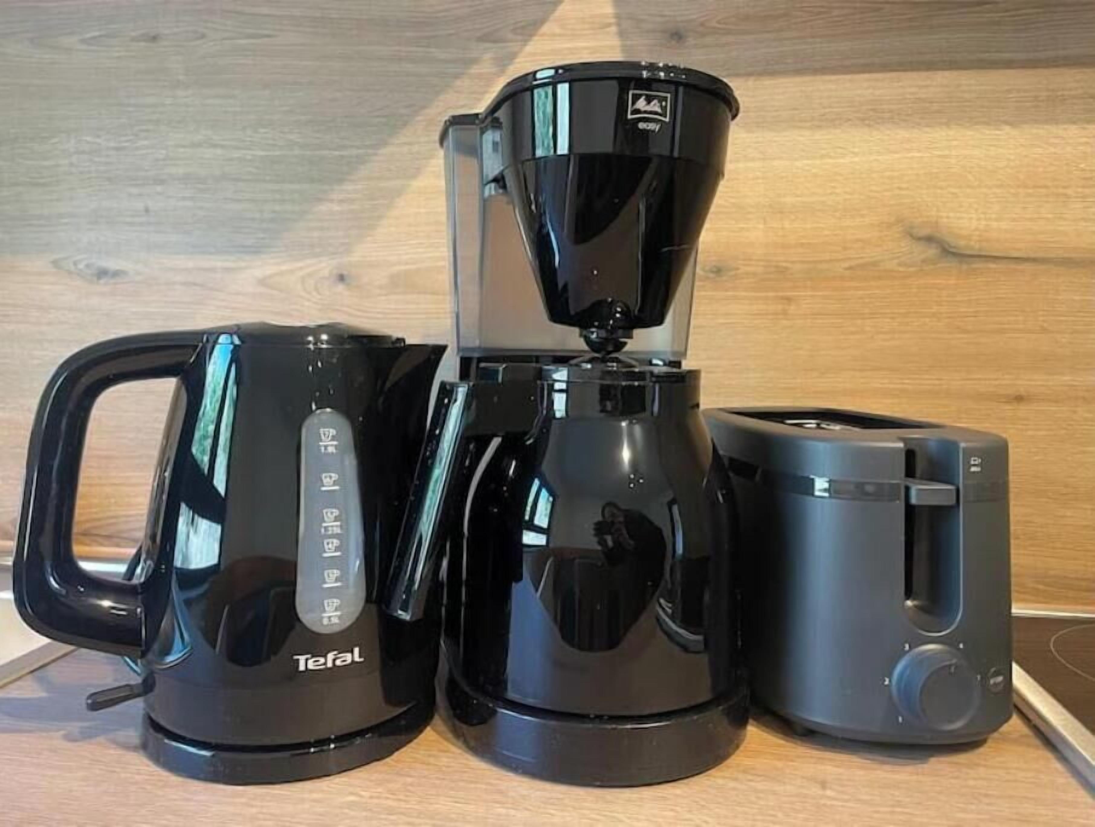 Une machine à café avec un bac de récupération, une cafetière et un grille-pain, le tout posé sur une surface en bois.