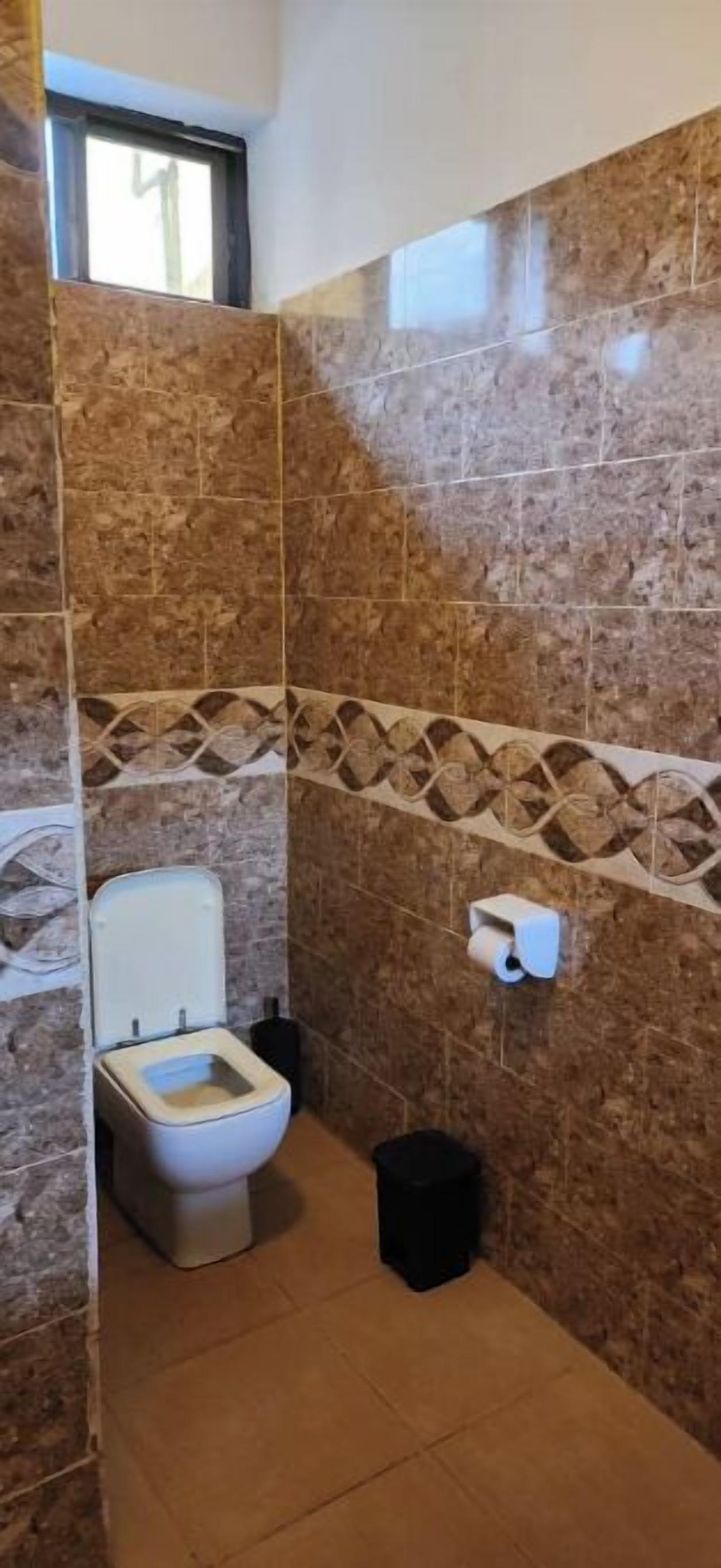 A bathroom with a toilet, a trash bin, and a wall-mounted toilet paper holder.