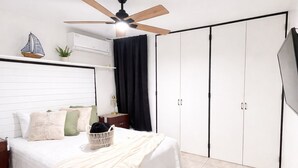 Een slaapkamer met een bed, een plafondventilator, een televisie, een kledingkast en een kleine plant.