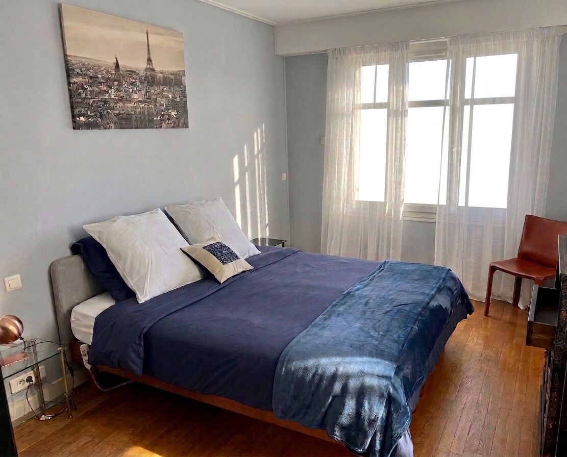 A bedroom with a bed, a chair, a desk, and a window with curtains.