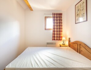 A bedroom with a bed, a window with a plaid curtain, a bedside lamp, and a wall-mounted picture. - Mountain Apartment With Alpine Comfort (Saint-Sorlin-d'Arves)