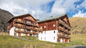 En flerlagsbygning i træ med altaner, beliggende foran et bjerglandskab.