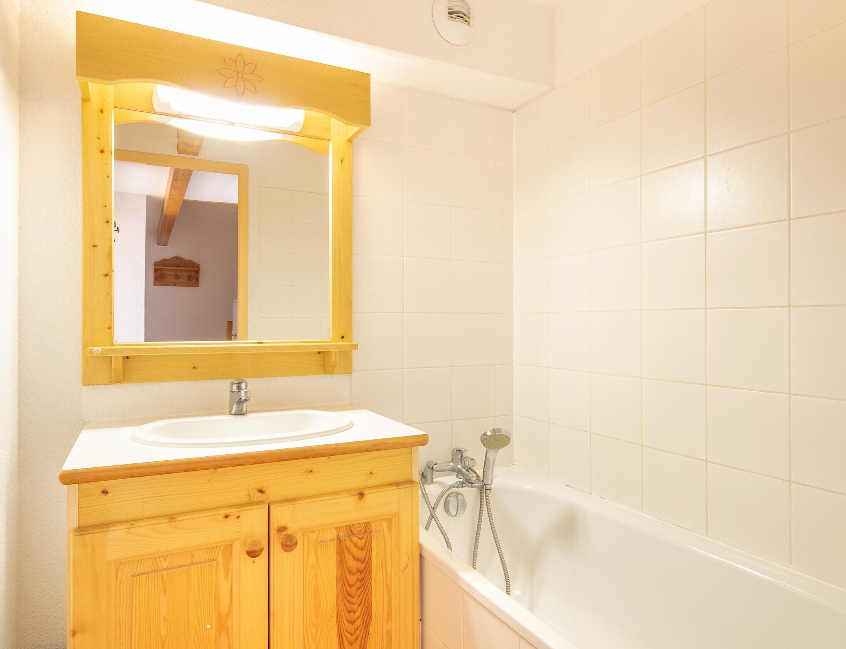 A bathroom with a wooden vanity, a white sink, a mirror, and a bathtub.