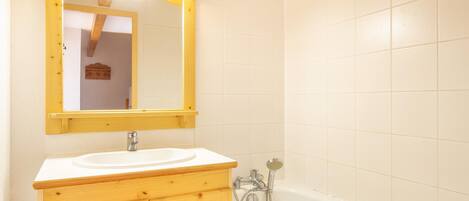 A bathroom with a wooden vanity, a white sink, a mirror, and a bathtub.