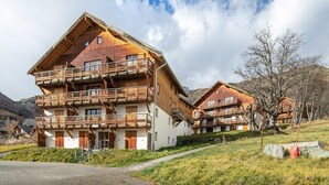 En flerplanschalet i træ med balkoner, beliggende i et bjerreigt landskab.