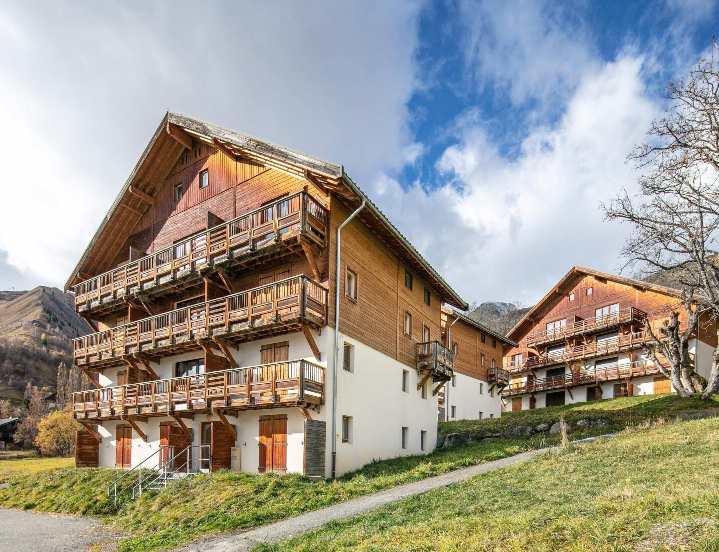 A wooden chalet with balconies, a steep roof, and a mountainous backdrop.