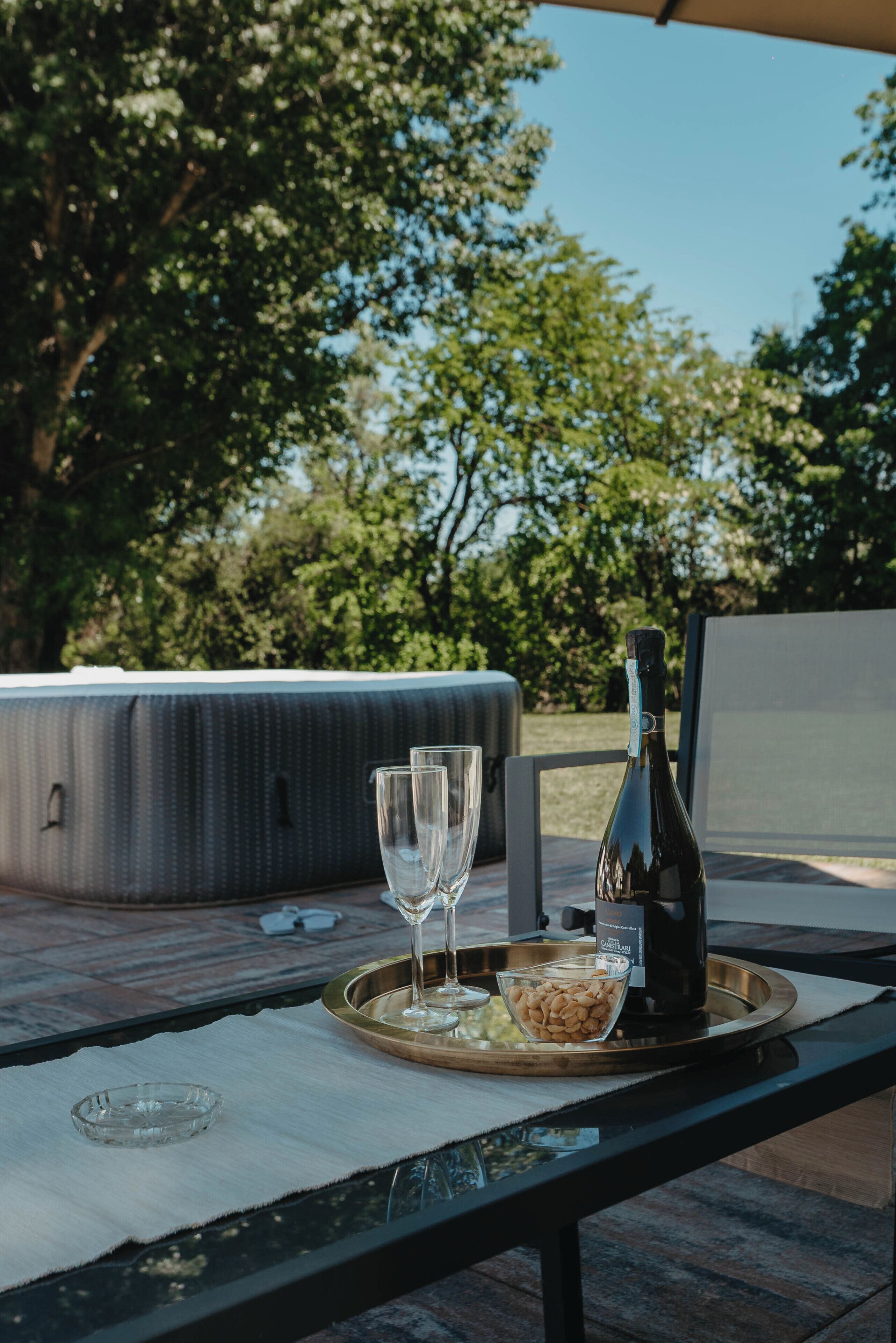 An outdoor seating area with a table, a bottle, glasses, and a bowl of nuts.