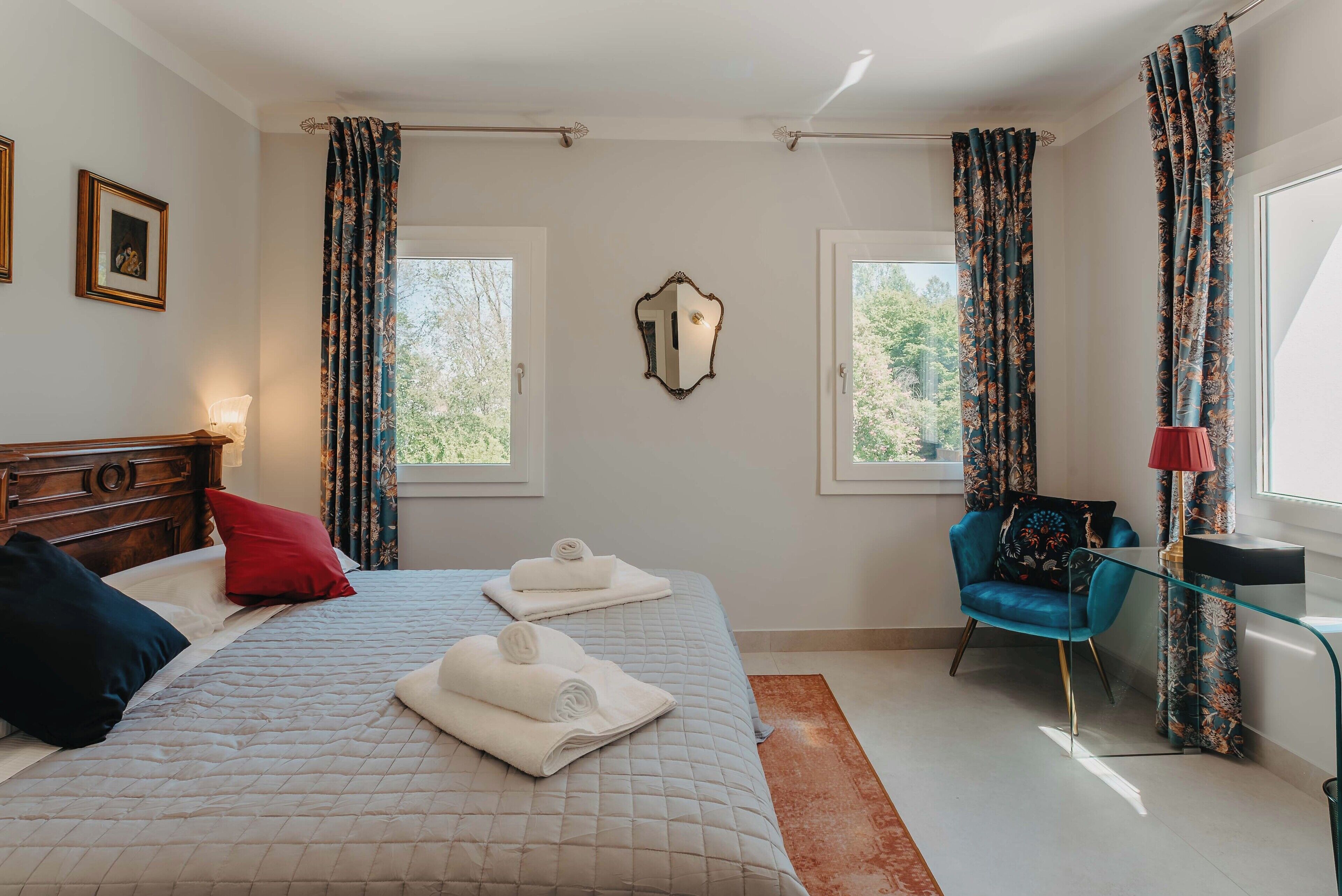 Habitación de hotel con cama, una silla, un espejo y dos ventanas.