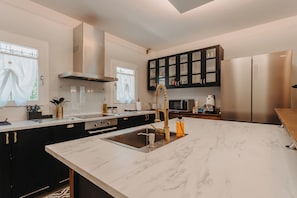 A modern kitchen with a marble countertop, stainless steel appliances, and black cabinetry. - Villa Freya | Private Wellness Retreat on the Sile River near Venice (Casale Sul Sile)