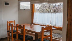 A dining area with a wooden table and chairs, a window with a view of trees, and a small window above the table. - NOTRO 2 Tero (San Carlos de Bariloche)