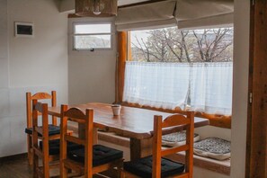 Un comedor con una mesa y sillas de madera, una ventana con vistas a árboles, y un ventanal pequeño sobre la mesa.