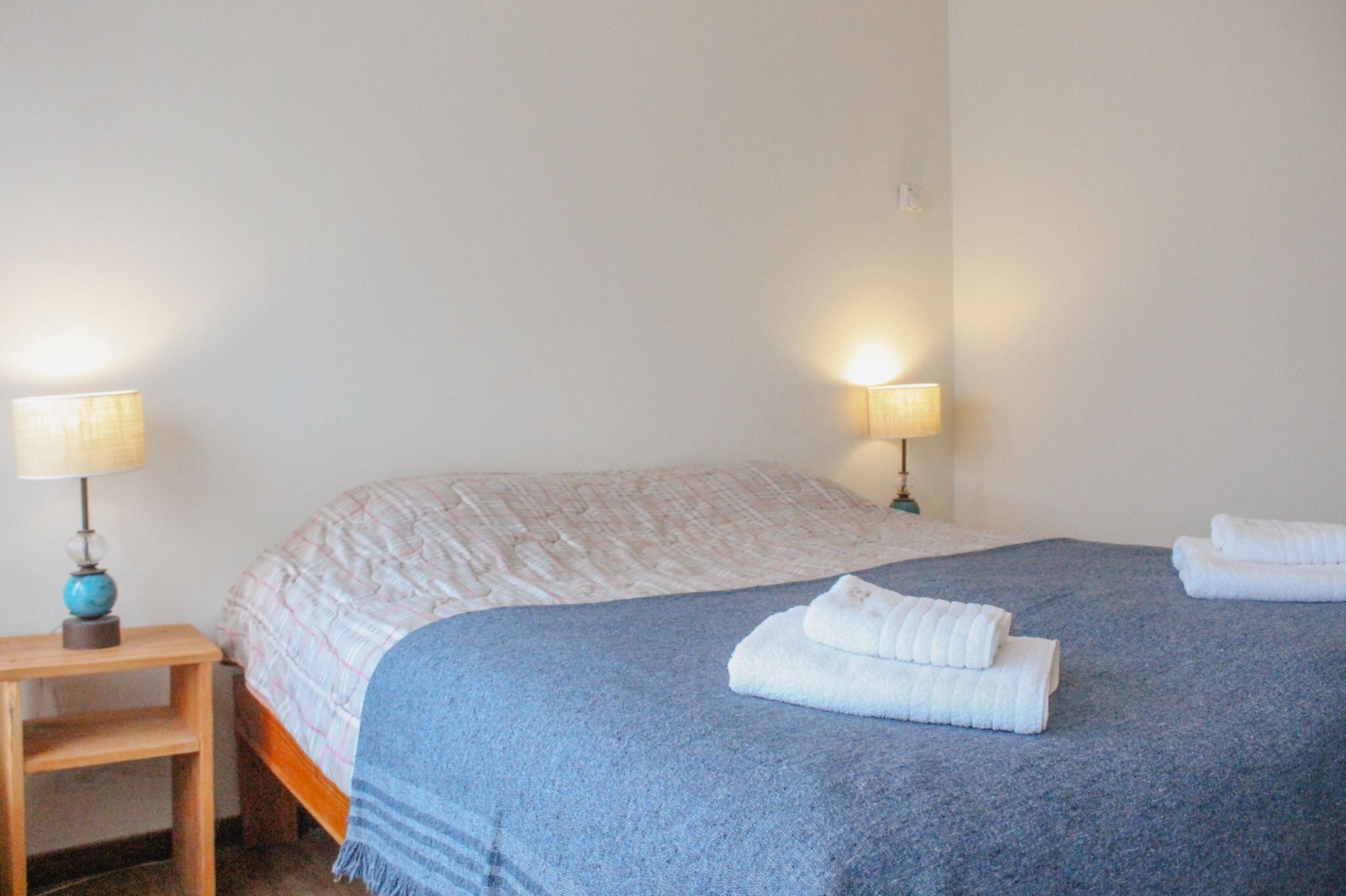 Ein ordentlich bezogenes Bett mit blauer Decke, zwei Nachttischlampen und einem Holznachttisch.