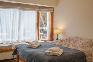 Une chambre d’hôtel avec un lit, deux serviettes enroulées, une lampe de chevet et une fenêtre avec des rideaux.