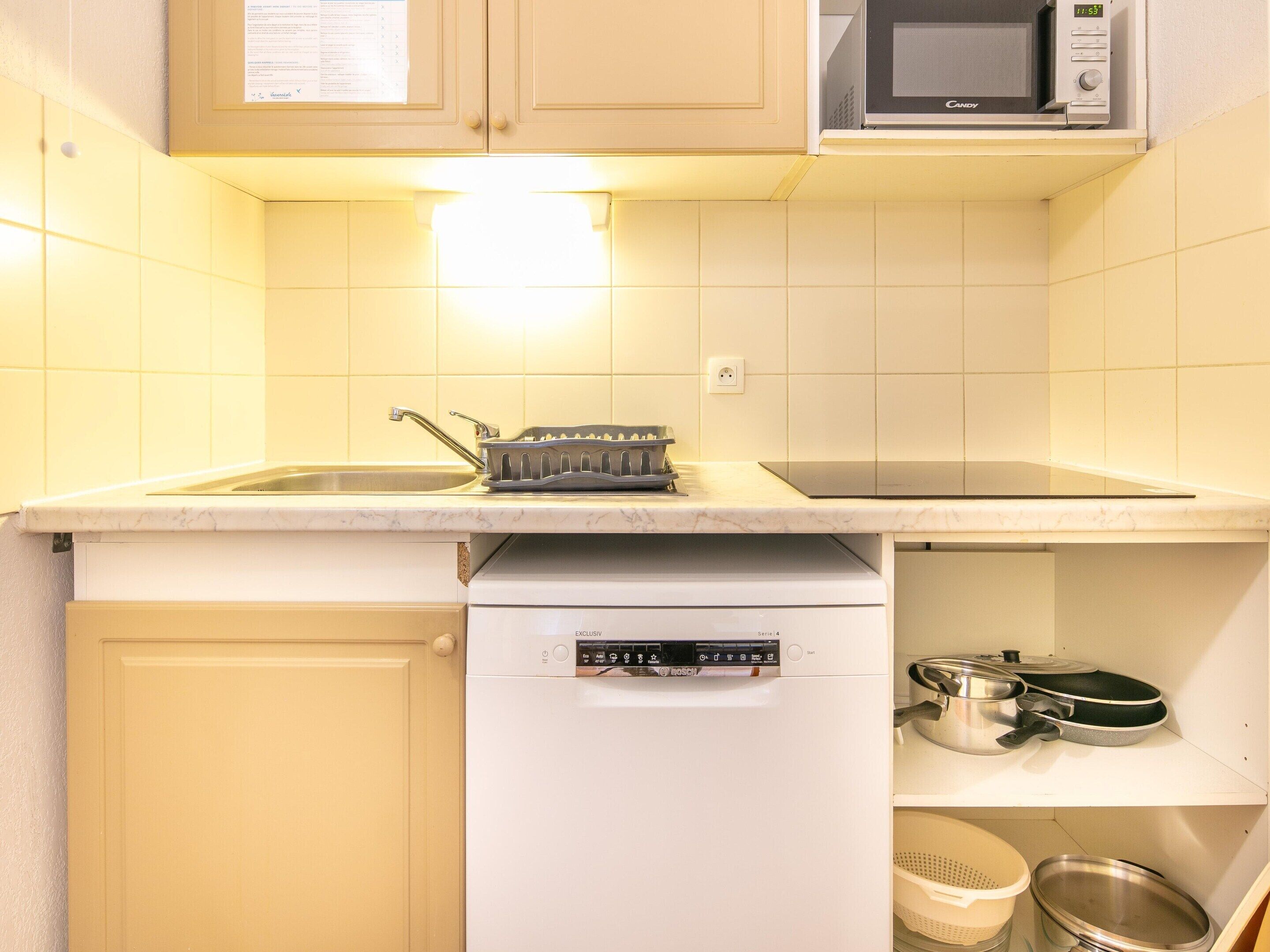 Een kleine keuken met een magnetron, spoelbak en vaatwasser.