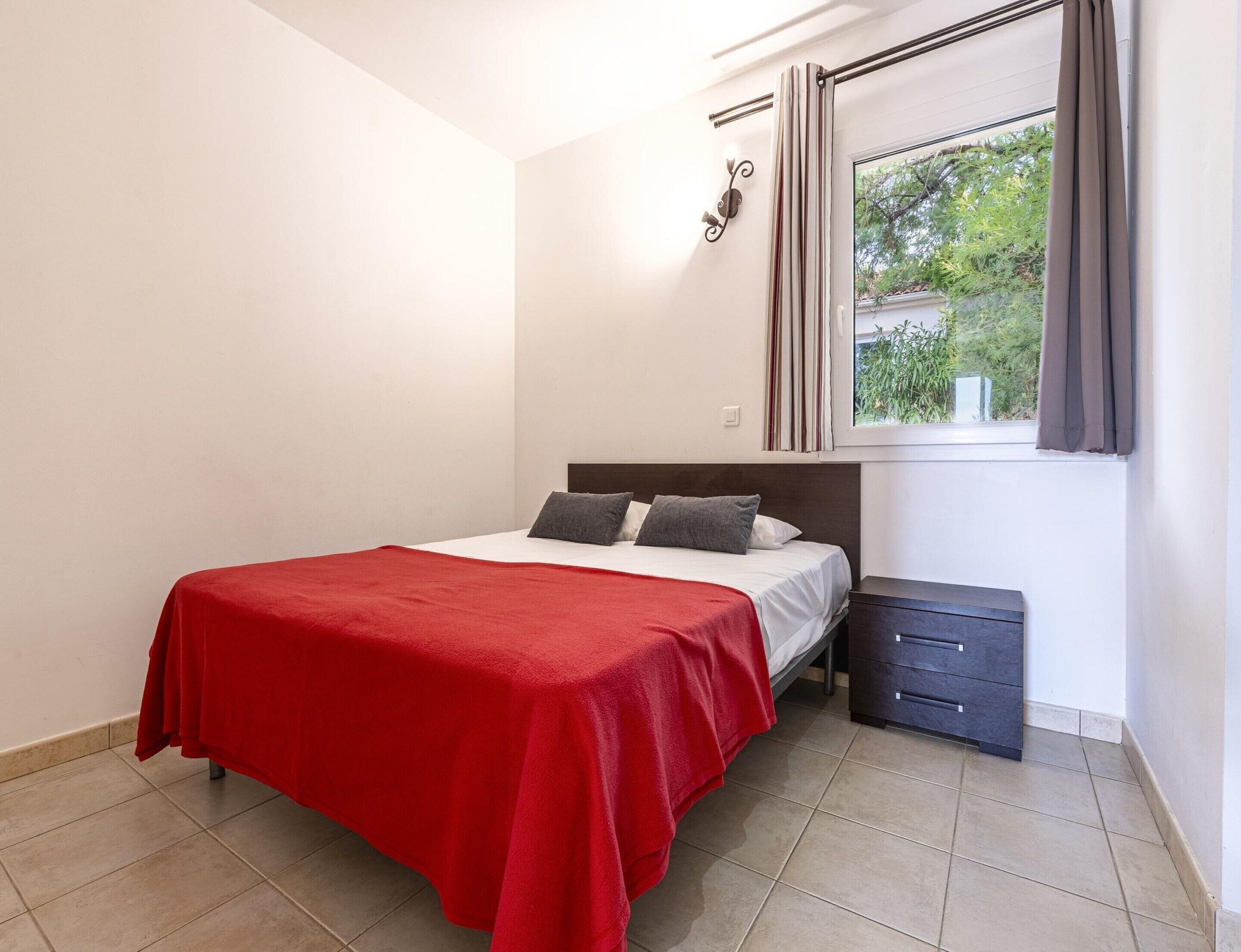 Une chambre à coucher avec un lit, une table de chevet, une fenêtre avec des rideaux et une vue sur la verdure.