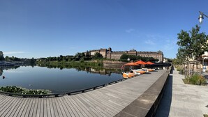 Una passeggiata lungofiume con un fiume tranquillo, una passerella in legno e un grande edificio sullo sfondo.
