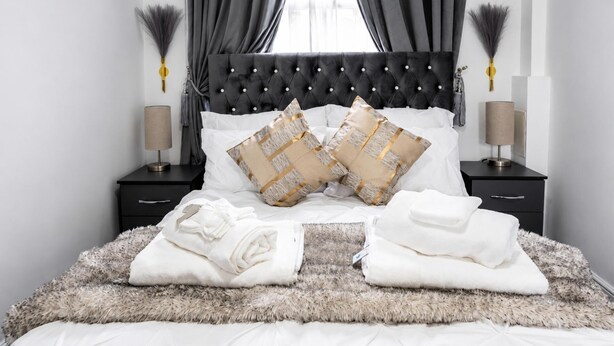 Uma cama bem arrumada com duas almofadas decorativas, um tapete macio e duas mesas de cabeceira com abajures.