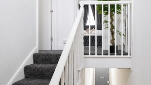 Uma escada com corrimão branco leva a um quarto com cama e planta.