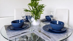 Uma mesa de vidro redonda com tigelas azuis, copos de vinho e um vaso de planta.