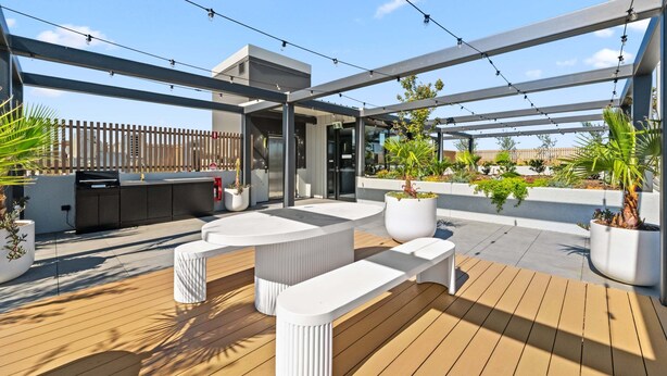 Una terraza en la azotea con mobiliario exterior, una parrilla y plantas en macetas.